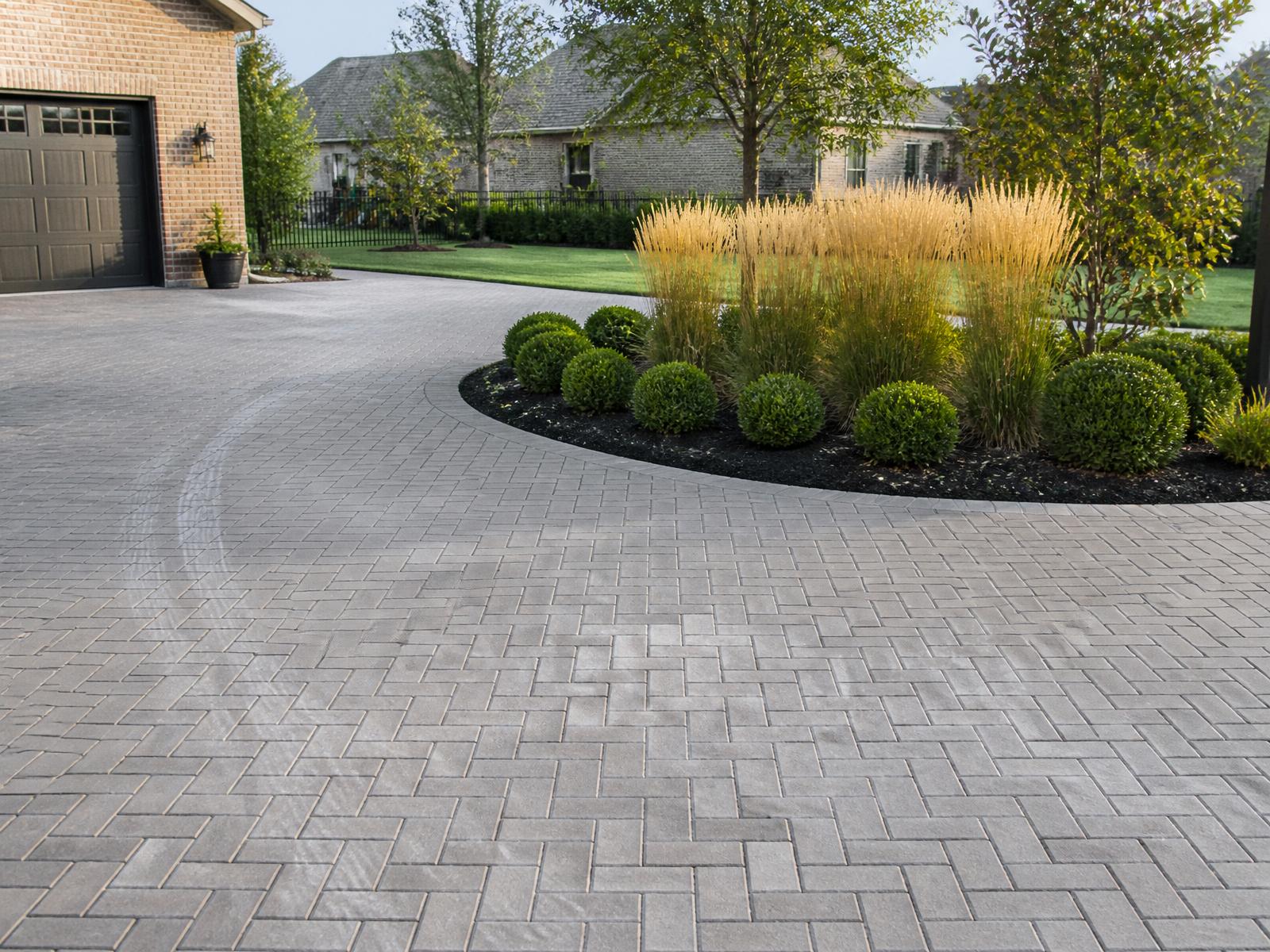 A herringbone paver driveway with planted island and ornamental grasses at a luxury Indiana home