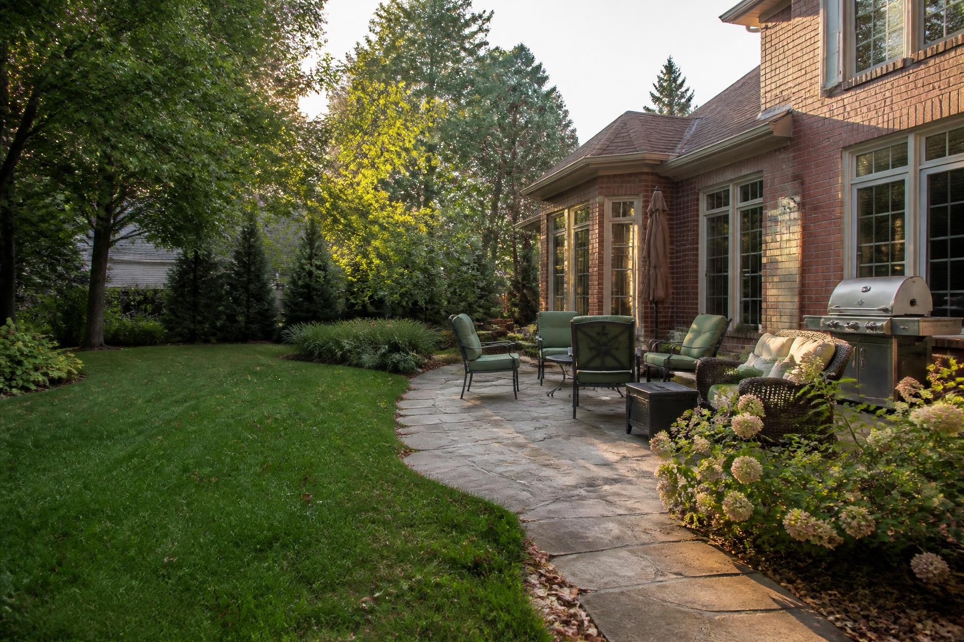 A luxury Indiana residential landscape with brick home, paver patio, hydrangeas and ornamental grasses at golden hour